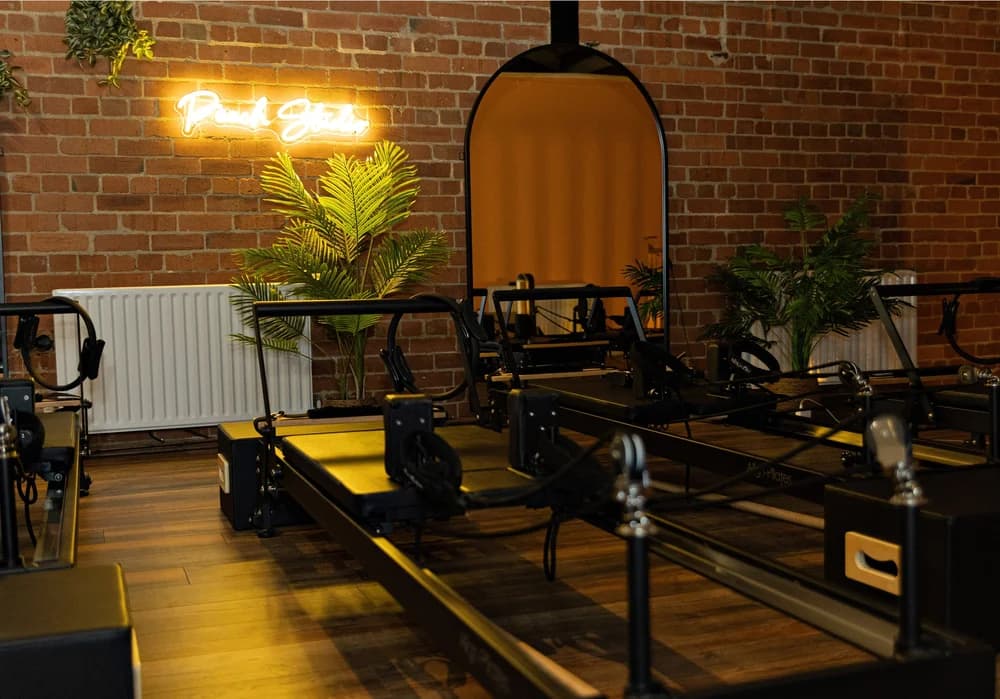 The studio floor at Peach Studio in Ripley: a row of reformers under the neon sign, with exposed brick and an arched mirror